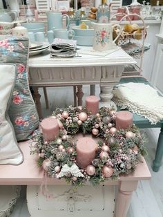 a pink table topped with lots of candles and wreaths next to a white chair