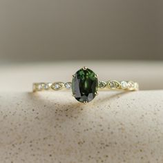 a ring with a green oval stone surrounded by white and yellow diamonds on a table