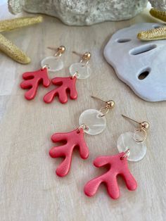 three pairs of pink and red earrings sitting on top of a wooden table next to starfish