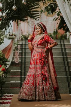 a woman in a red and gold bridal gown standing on steps with flowers around her neck