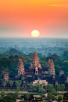 the sun is setting over an ancient city with many towers and trees in front of it