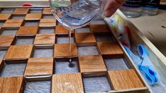 someone is pouring water into a wine glass on a wooden tray with squares and crosses