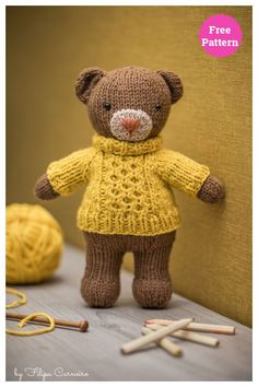 a knitted teddy bear wearing a yellow sweater next to knitting needles and crochet hooks