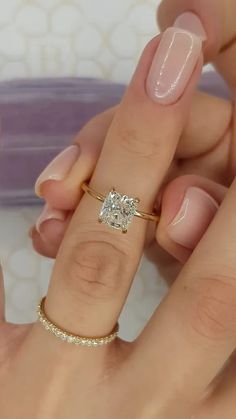 a woman's hand holding a ring with a diamond on it and the other hand