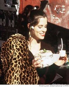 a woman sitting at a table with a sandwich and drink in her hand while talking on the phone