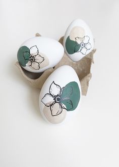 three painted eggs with flowers on them sitting in an egg carton, ready to be eaten