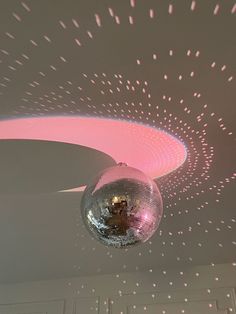 a disco ball hanging from the ceiling in a room with pink lights and white walls