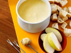 a bowl of soup, crackers and apples on a yellow tray with utensils