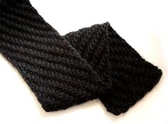 a black knitted scarf laying on top of a white surface