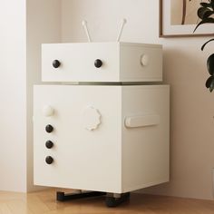 a white cabinet sitting on top of a wooden floor next to a potted plant