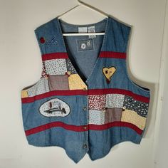 a blue jean vest with patchwork and patches on the front, hanging from a white wall