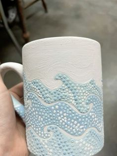 a hand holding a blue and white mug with waves on it's outside side