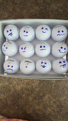 a dozen golf balls with faces drawn on them in a cardboard box sitting on a counter