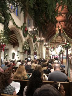 a church filled with people sitting in pews next to christmas wreath hanging from the ceiling