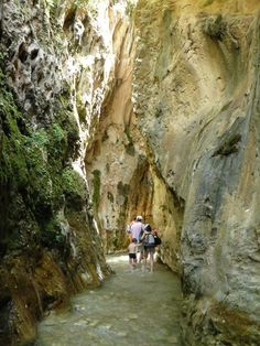 two people are walking through a narrow canyon