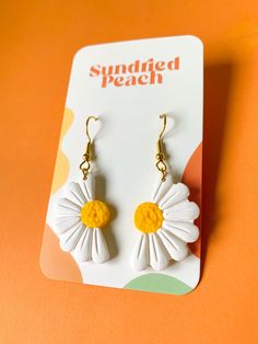 a pair of white and yellow flower earrings on an orange background with the words sunflower peach