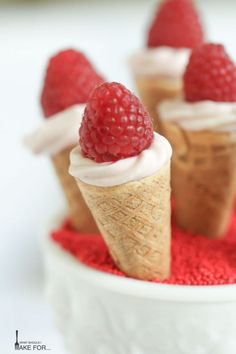 three ice cream cones with raspberries on top in a white bowl filled with red sprinkles