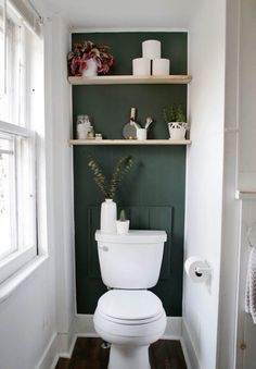 a white toilet sitting in a bathroom next to a green wall with shelves above it