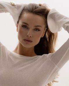 a woman with her hair in a ponytail and wearing a white sweater is posing for the camera