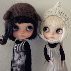 two dolls standing next to each other wearing knitted hats and dress clothes, one in black and the other in white