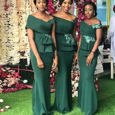 two women in green dresses standing next to each other on the grass with flowers behind them