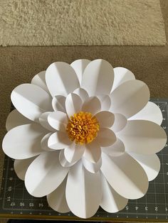 a large white paper flower sitting on top of a cutting board next to a ruler