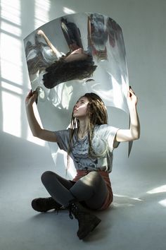 a woman sitting on the ground with her reflection in a mirror