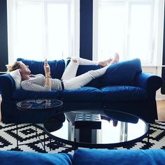 a woman laying on top of a blue couch in a living room next to a window