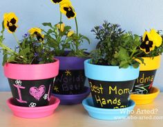 four flower pots with flowers in them painted on the sides and chalkboard writing on the bottom