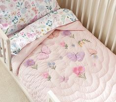 a crib bed with a pink quilt and butterflies on the sheets, along with a pillow