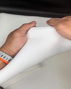 two hands holding an electronic device on top of a white sheet with orange band around it