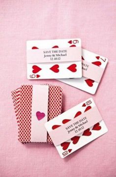 four playing cards with hearts on them sitting on a pink tablecloth, one is red and the other is white