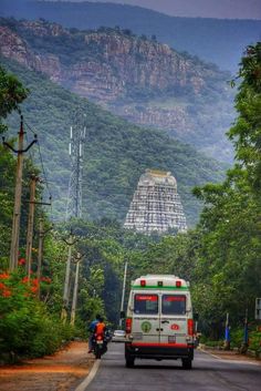 an ambulance is driving down the road in front of a large stone structure on top of a mountain