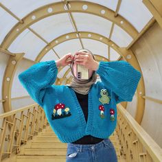 a woman taking a photo with her cell phone wearing a blue knitted cardigan