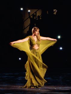 a woman in a yellow dress standing on stage with her arms spread out to the side