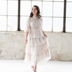 a woman standing in front of a window wearing a dress with sheer lace on it