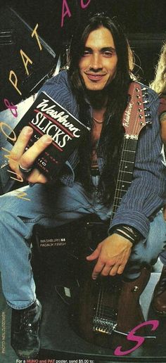 a man with long hair sitting on a chair holding a book and guitar in his hands