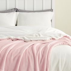 an unmade bed with white sheets and pink blankets on it's headboard