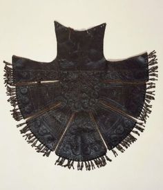 an old black piece of cloth with fringes on the bottom and sides, sitting on a white surface