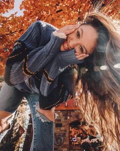 a beautiful young woman posing for a photo in front of some trees with fall leaves