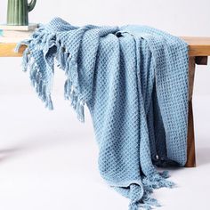 a blue crocheted blanket sitting on top of a wooden bench next to a vase