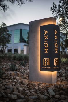 a sign that is sitting on some rocks in the dirt and grass with a building in the background