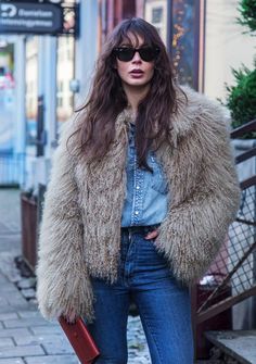 a woman standing on the sidewalk wearing jeans and a fur coat