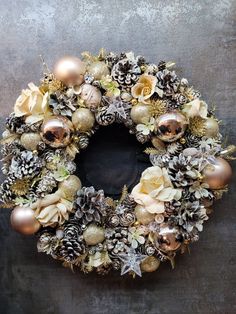 a christmas wreath with pine cones, ornaments and other decorations on a gray wall background