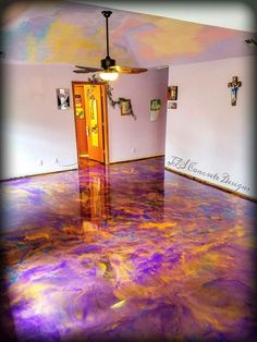 an empty room with purple and yellow paint on the floor, ceiling fan in center