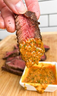 a hand holding up a piece of steak with dipping sauce