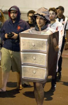 a man dressed up like a dresser walking down the street with people behind him looking on