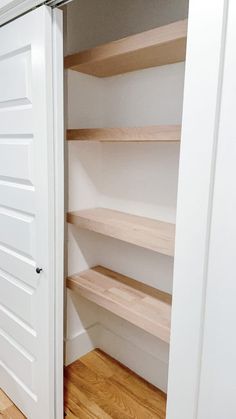 an empty closet with wooden shelves and white walls, along with hard wood flooring