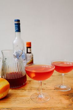 two glasses filled with liquid sitting on top of a wooden table next to an orange