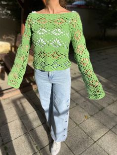 a woman walking down a sidewalk wearing jeans and a green crochet top with bell sleeves